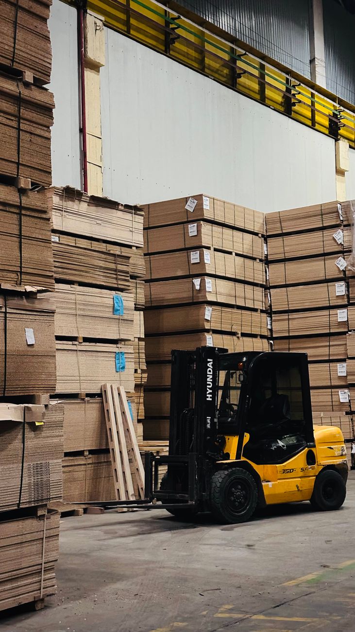 En gul gaffeltruck mellem stabler af plader i et lager